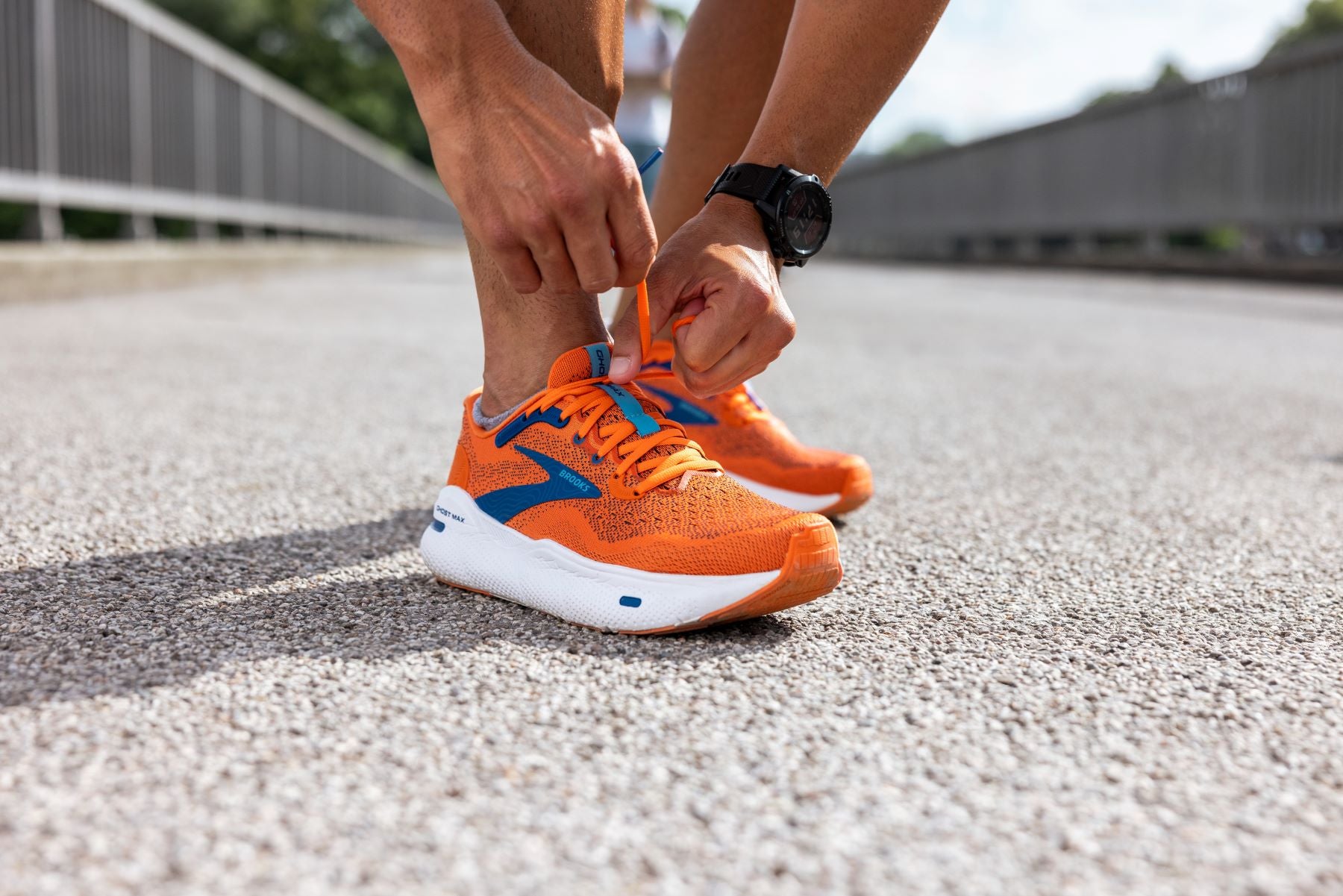 Up close view of a runner's hands tying the shoe laces of his Orange Brooks running shoe.